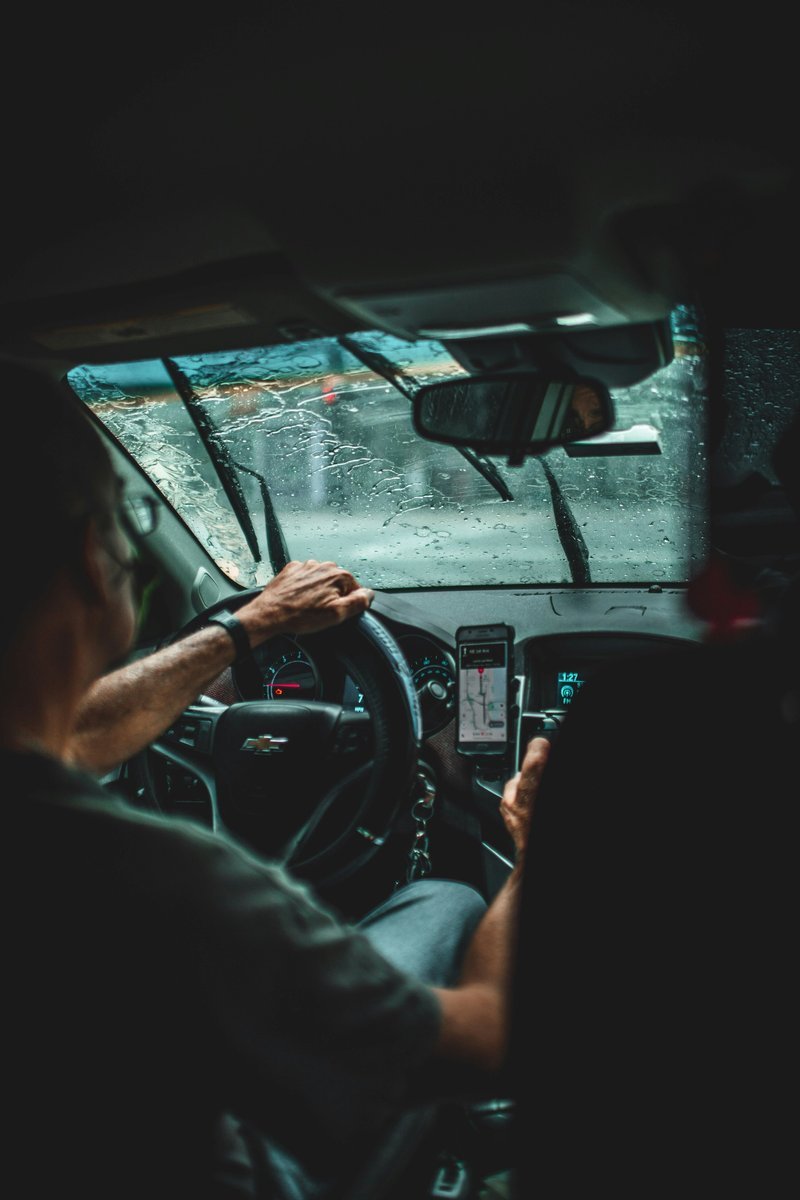 Motorista da Uber dirigindo carro na chuva com app de corridas aberto