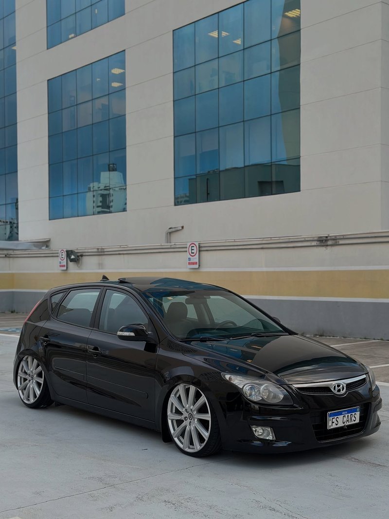 Hyundai i30 preto com rodas aro 20 e suspensão a ar em estacionamento com vidro azul ao fundo