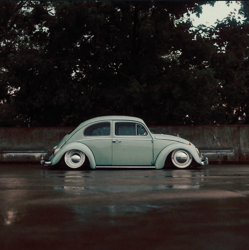 Fusca de lado com suspensão rebaixada em rua molhada