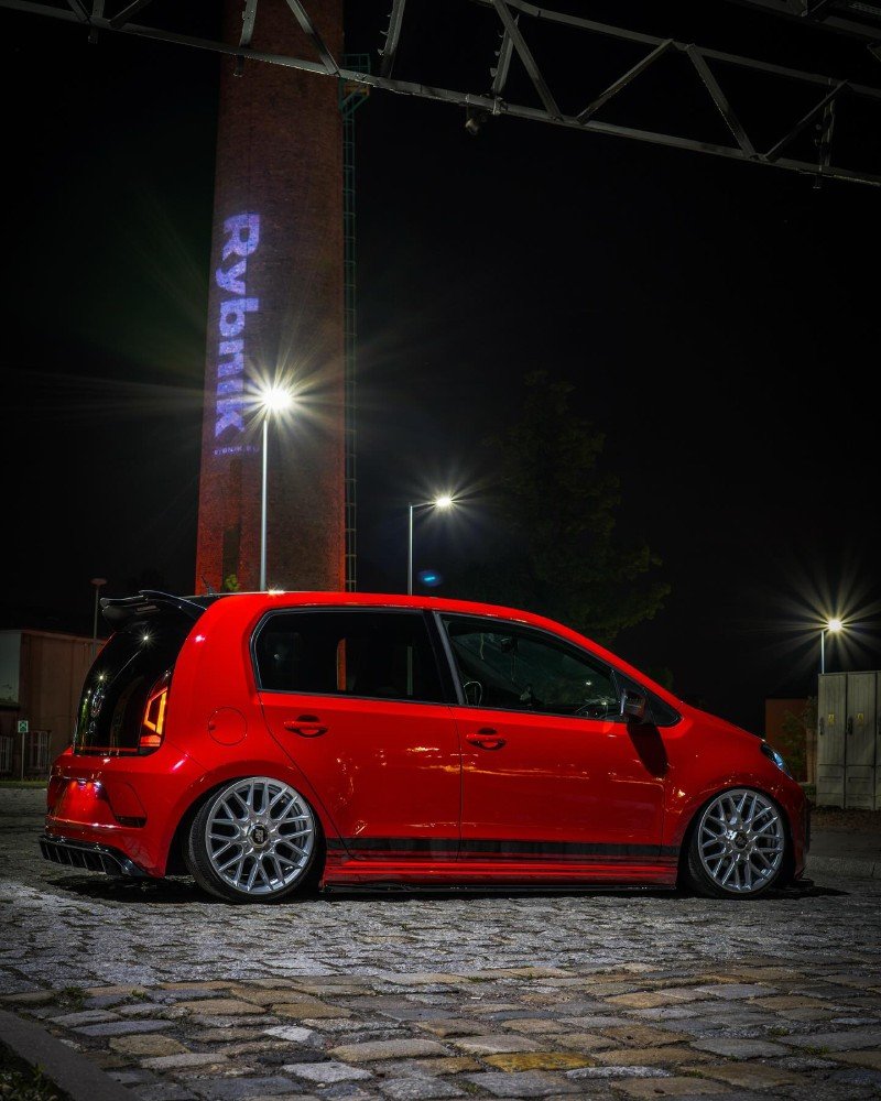 VW Up vermelho com rodas esportivas em cenário urbano à noite