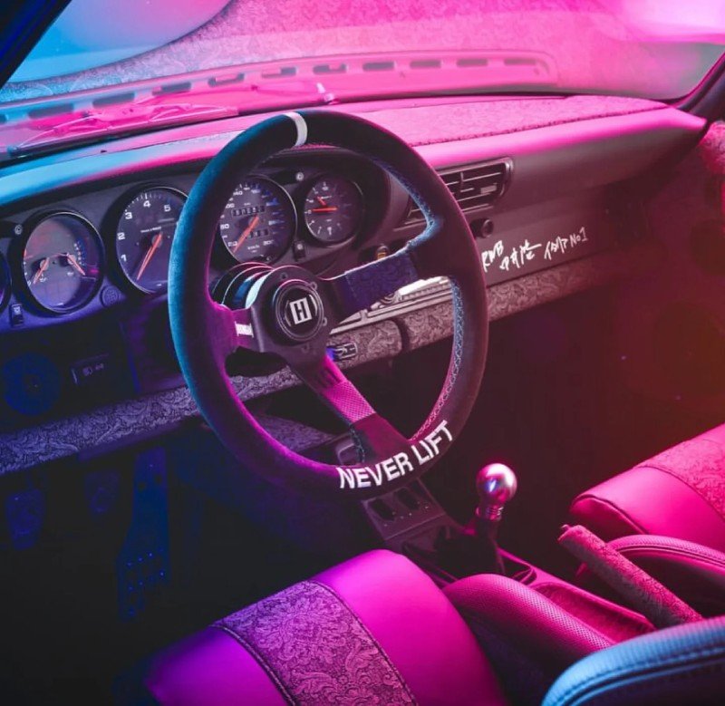 Interior do Porsche 964 RWB com volante esportivo e bancos personalizados sob iluminação neon