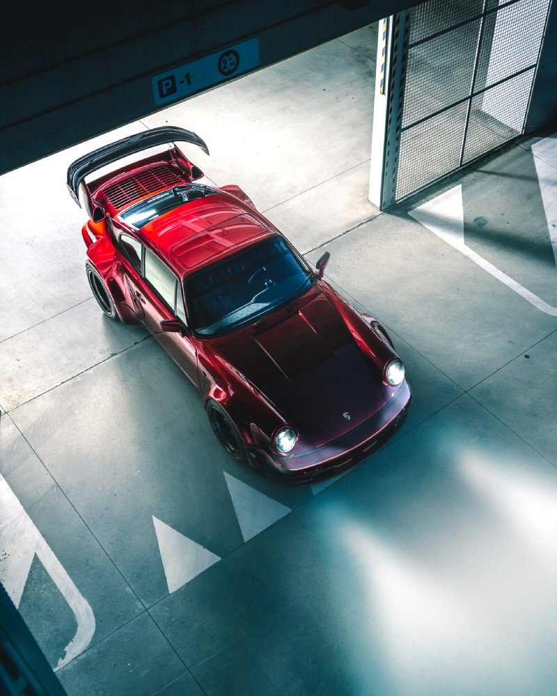 Porsche 964 RWB vermelho visto de 3/4 superior em piso de concreto, paralamas alargados