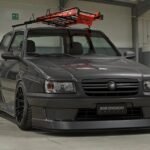 Fiat Uno escada rebaixado cinza com bodykit widebody, rodas pretas e escada laranja no teto em pavilhão