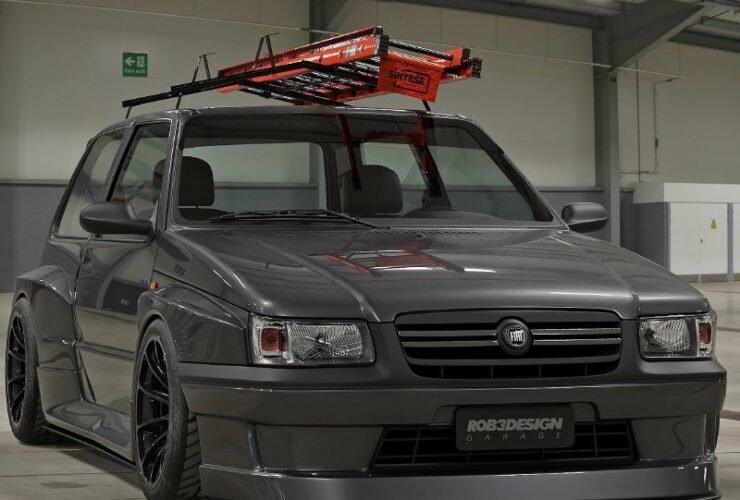 Fiat Uno escada rebaixado cinza com bodykit widebody, rodas pretas e escada laranja no teto em pavilhão