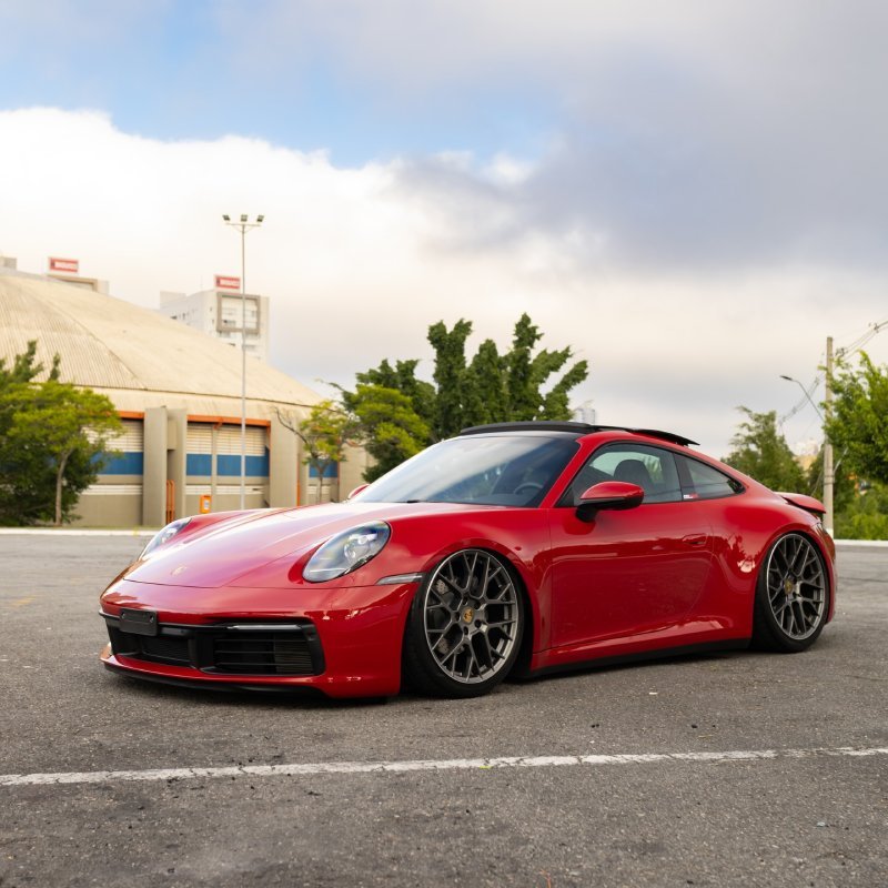 Porsche 911 Carrera 992 vermelho rebaixado com suspensão a ar visto de lado em estacionamento