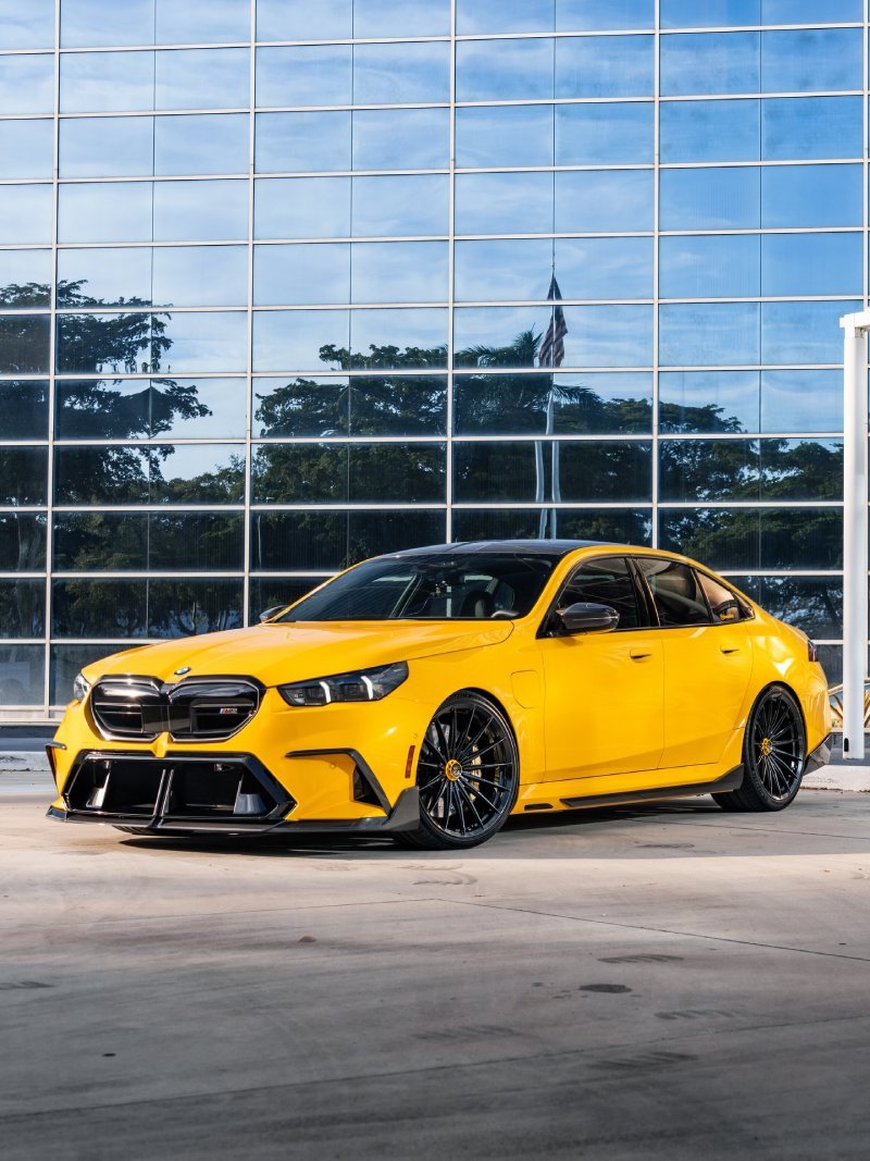 BMW M5 G90 amarelo rebaixado com rodas Vossen aro 22 em frente a prédio envidraçado