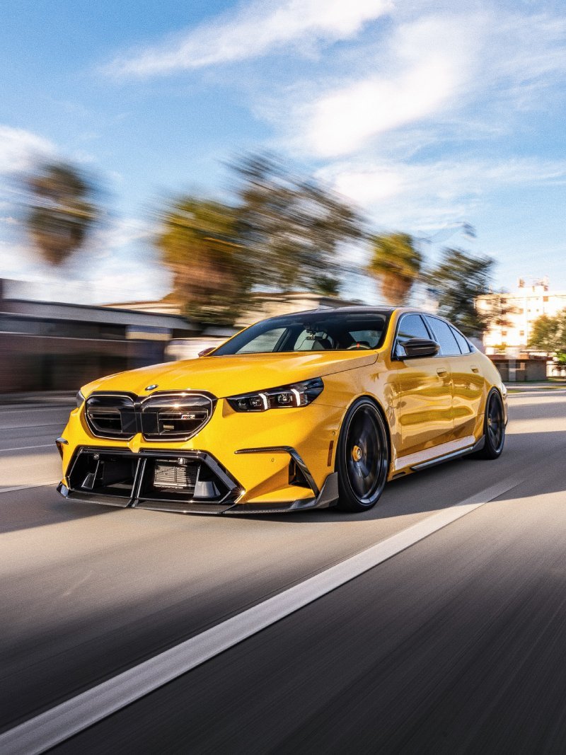BMW M5 G90 amarelo rebaixado em movimento na rua com fundo borrado