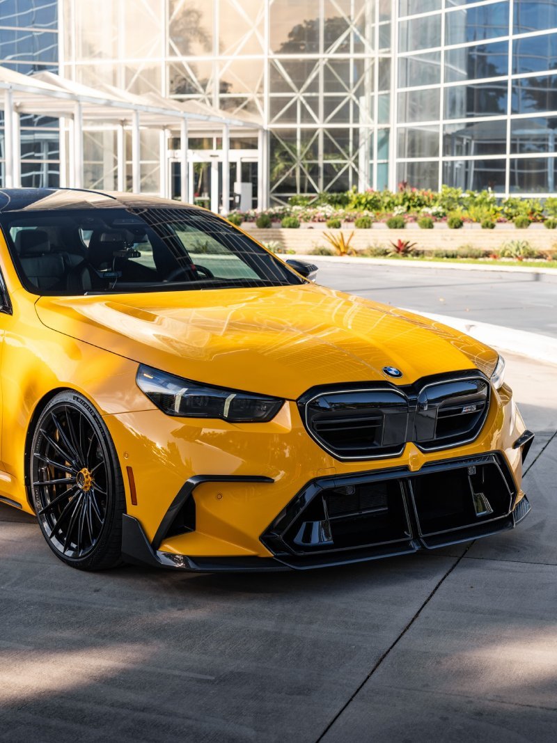 Close da dianteira do BMW M5 G90 amarelo com grade preta e rodas Vossen
