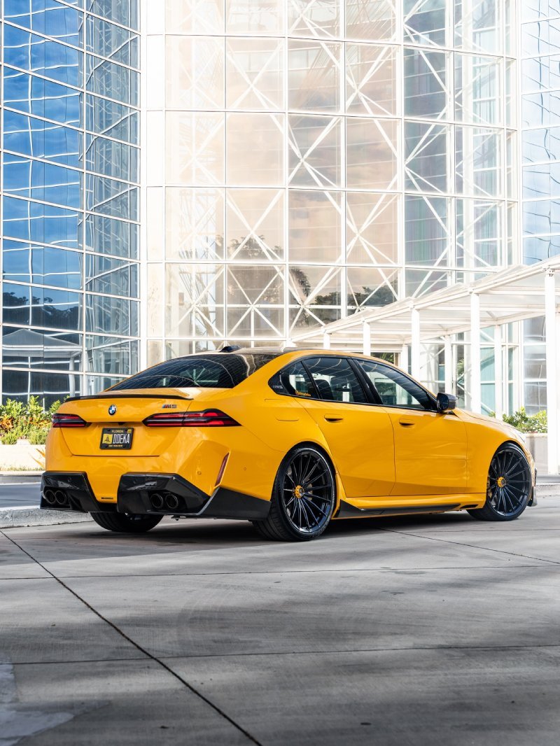 Traseira da BMW M5 G90 amarela rebaixada com difusor esportivo e quatro saídas de escape