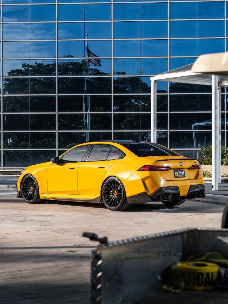 Visão traseira em três quartos da BMW M5 G90 amarela rebaixada estacionada