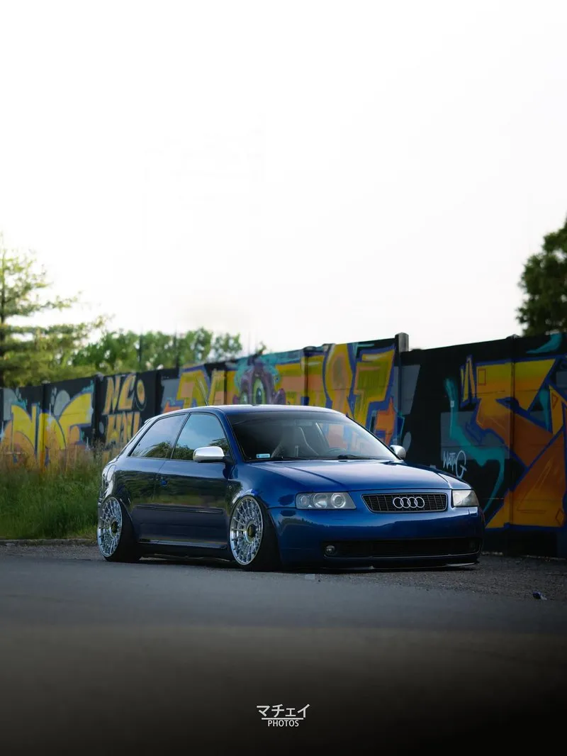 Lateral do Audi A3 azul com fitment agressivo e rodas Rotiform Audi A3 azul visto de lado com rodas Rotiform e fundo grafitado