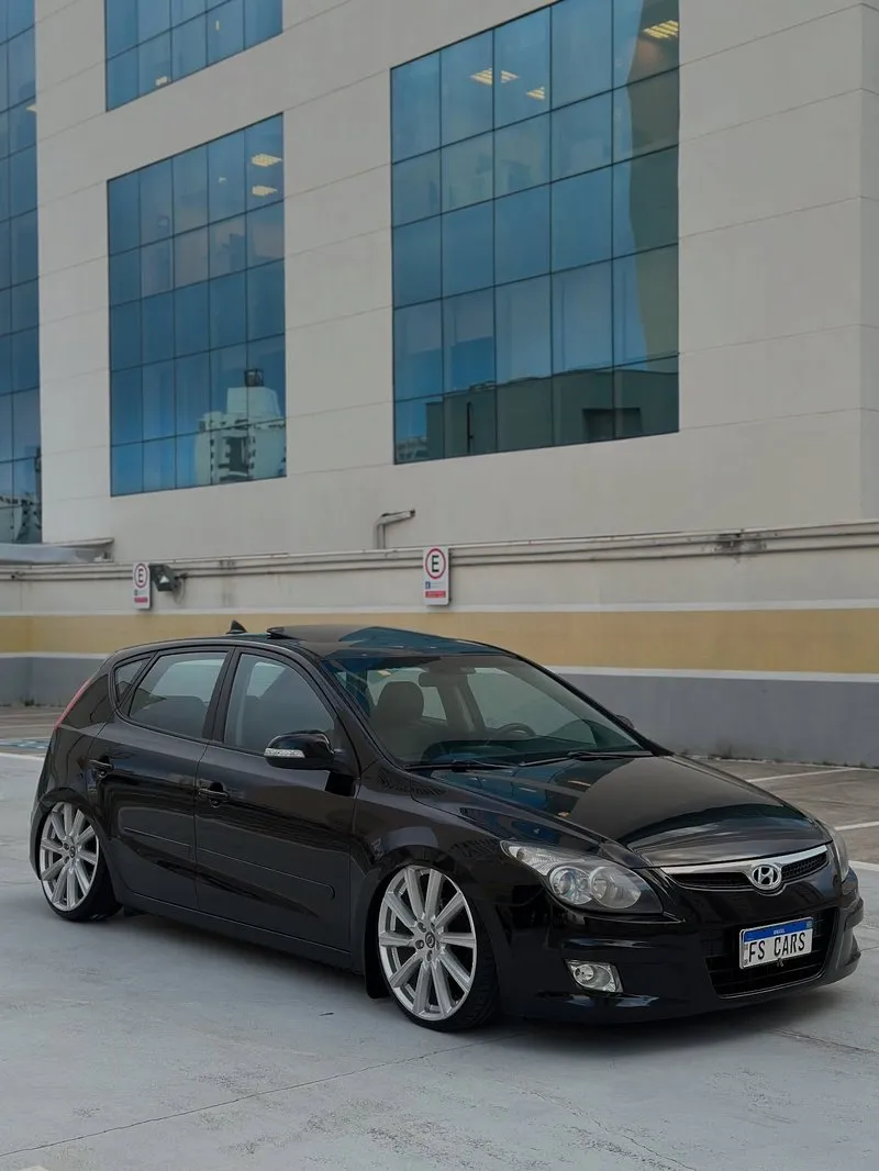 Hyundai i30 preto com rodas aro 20 e suspensão a ar em estacionamento com vidro azul ao fundo