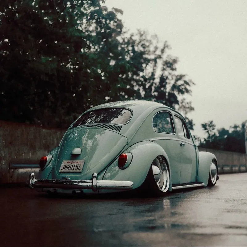 Fusca rebaixado com rodas tala larga em ambiente urbano molhado