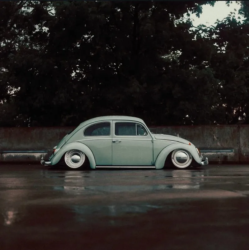 Fusca de lado com suspensão rebaixada em rua molhada