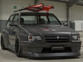 Fiat Uno escada rebaixado cinza com bodykit widebody, rodas pretas e escada laranja no teto em pavilhão